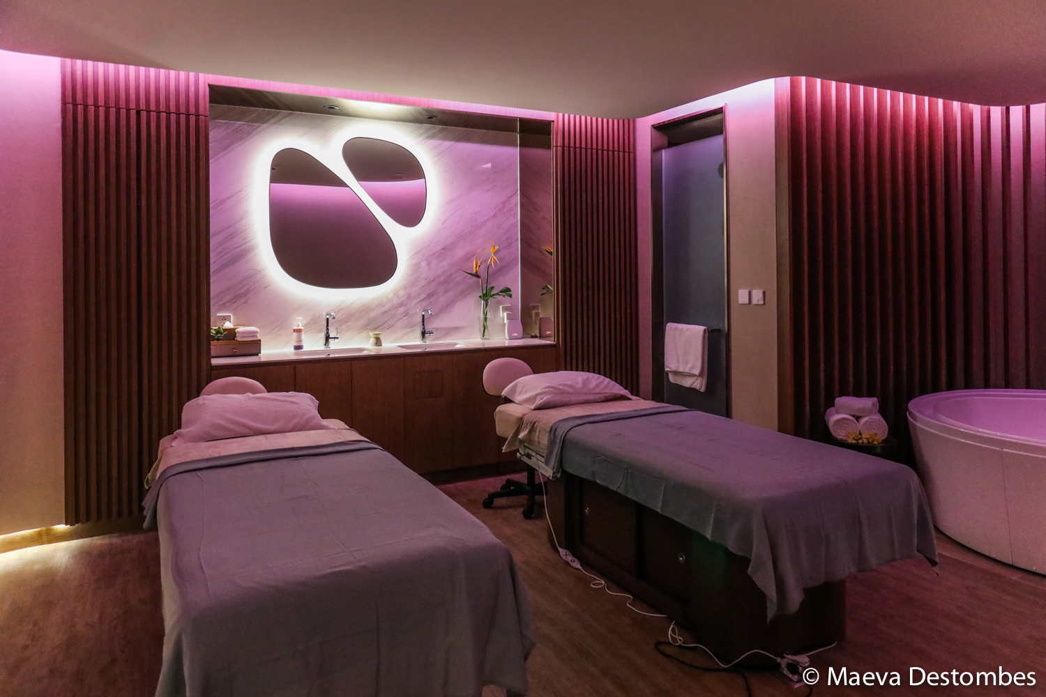 Une salle du spa dans les tons mauve avec deux tables de massages et deux miroirs arrondis.