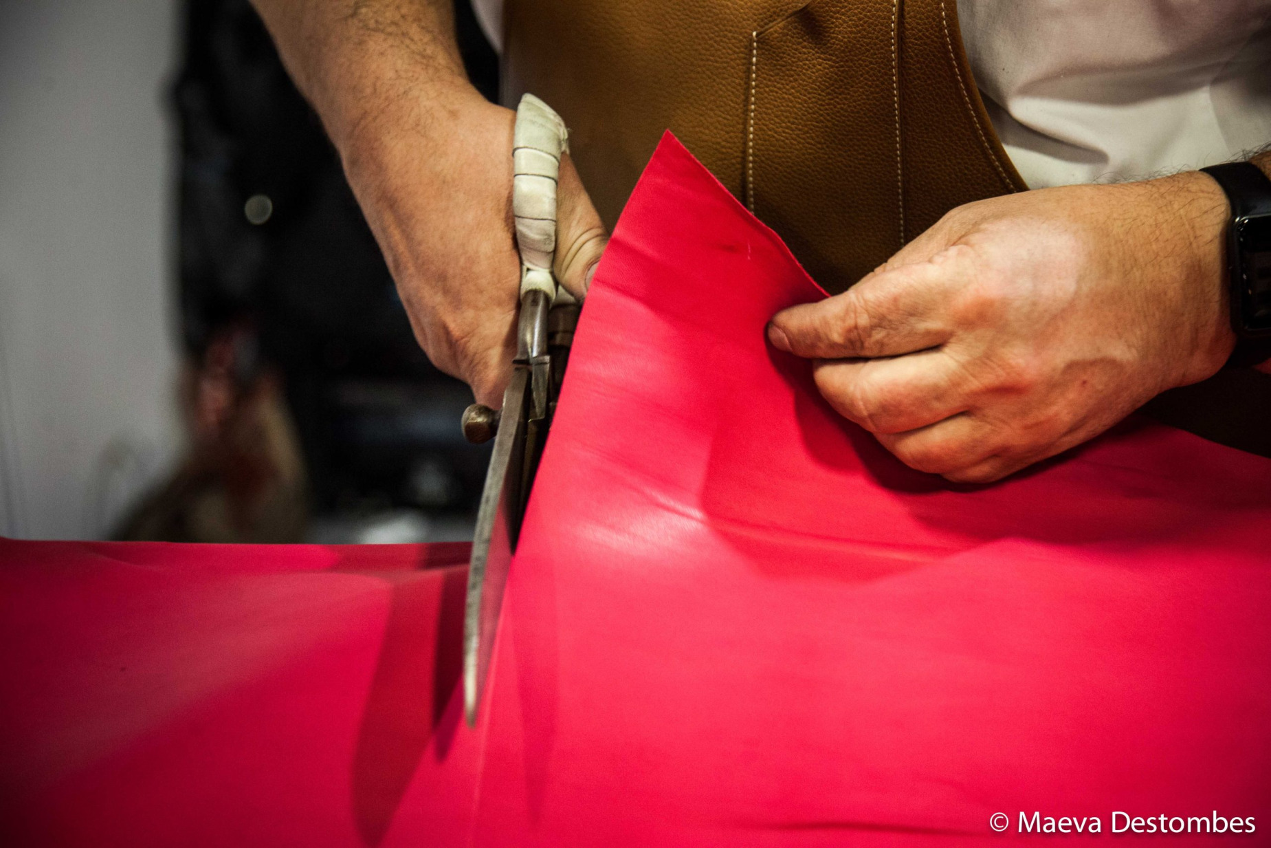 Un homme en train de couper du cuir rose fuchsia à l'aide de ciseaux.