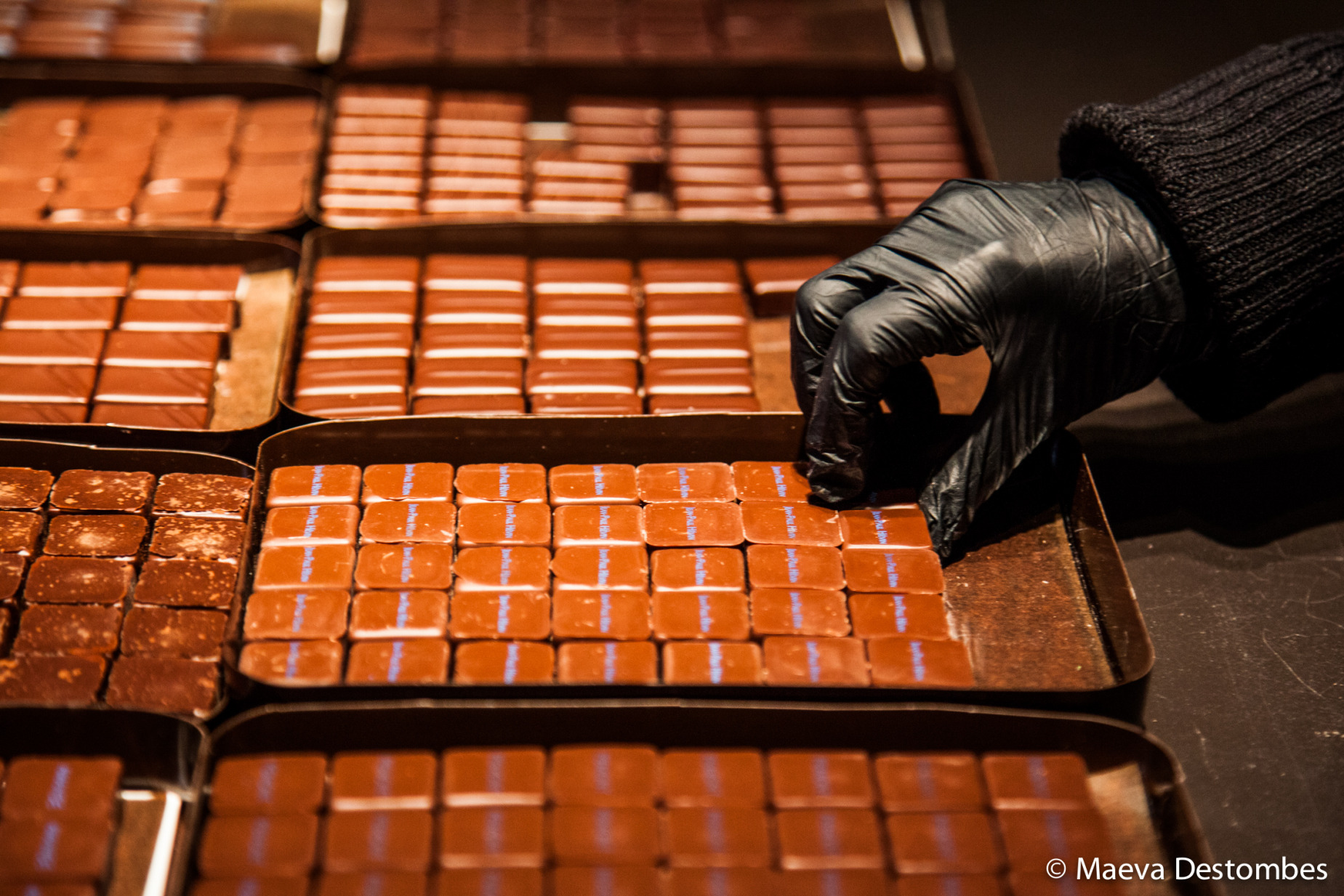 Une main ganté de noir range les bonbons au chocolat avec soin et délicatesse.