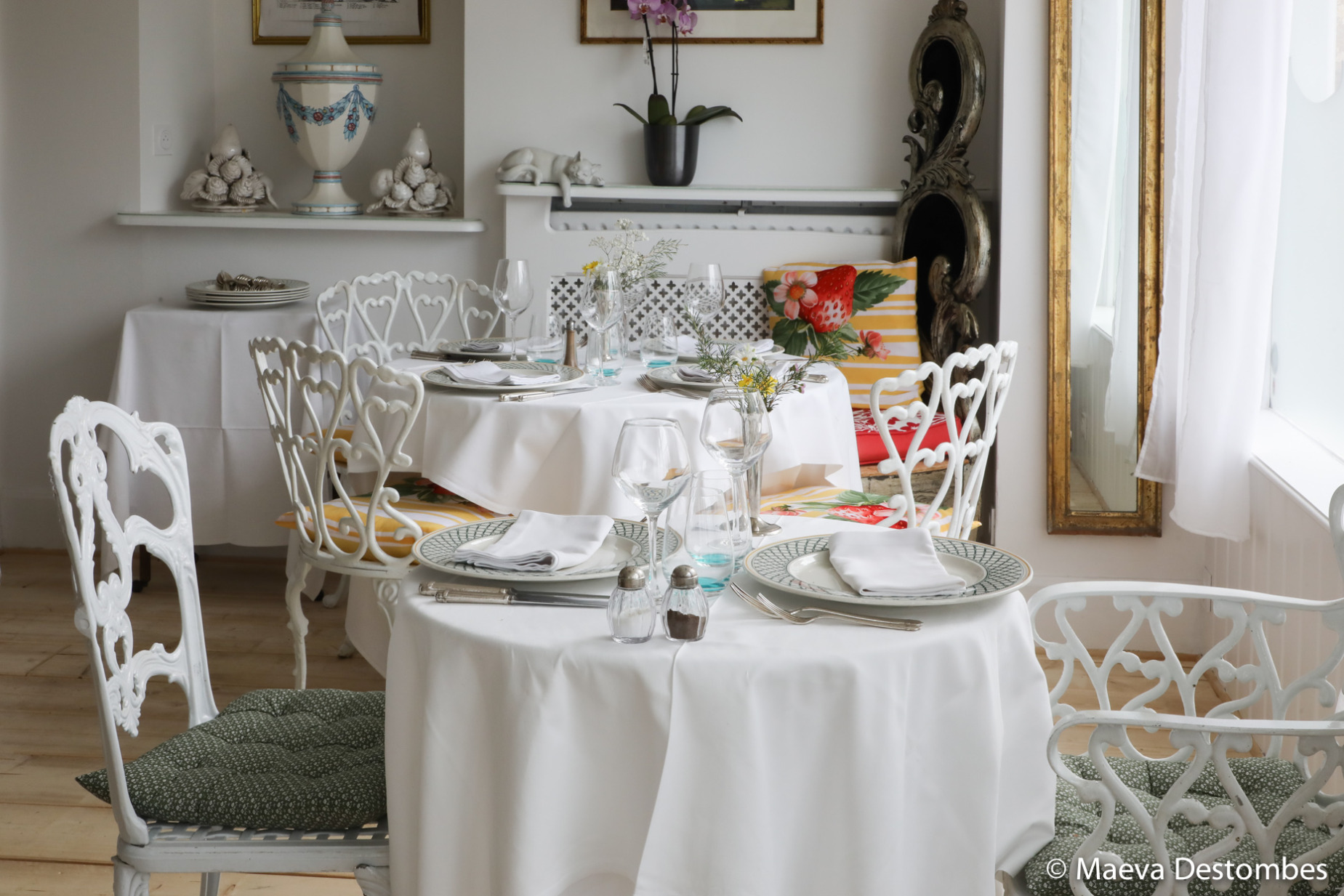 Des chaises blanches en fer forgé, des coussins colorés à motifs exotiques et une vaisselle soignée créent une ambiance chaleureuse et dépaysante.